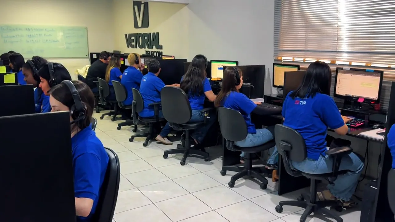 Time da Vetorial Telecom trabalhando no escritório, com o logo da empresa na parede.